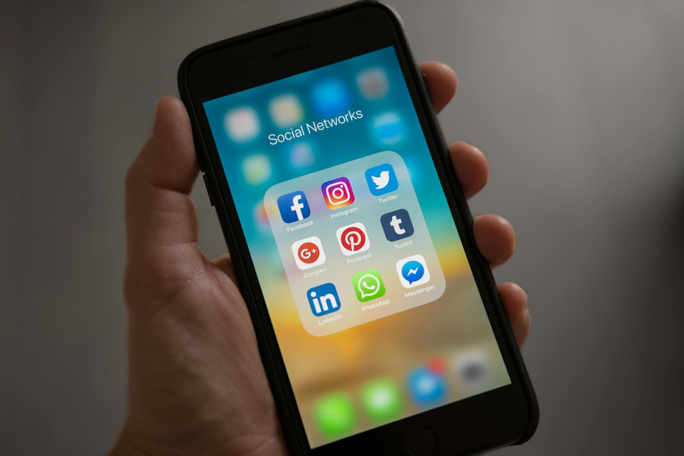Persona sosteniendo smartphone con carpeta de aplicaciones de redes sociales en pantalla
