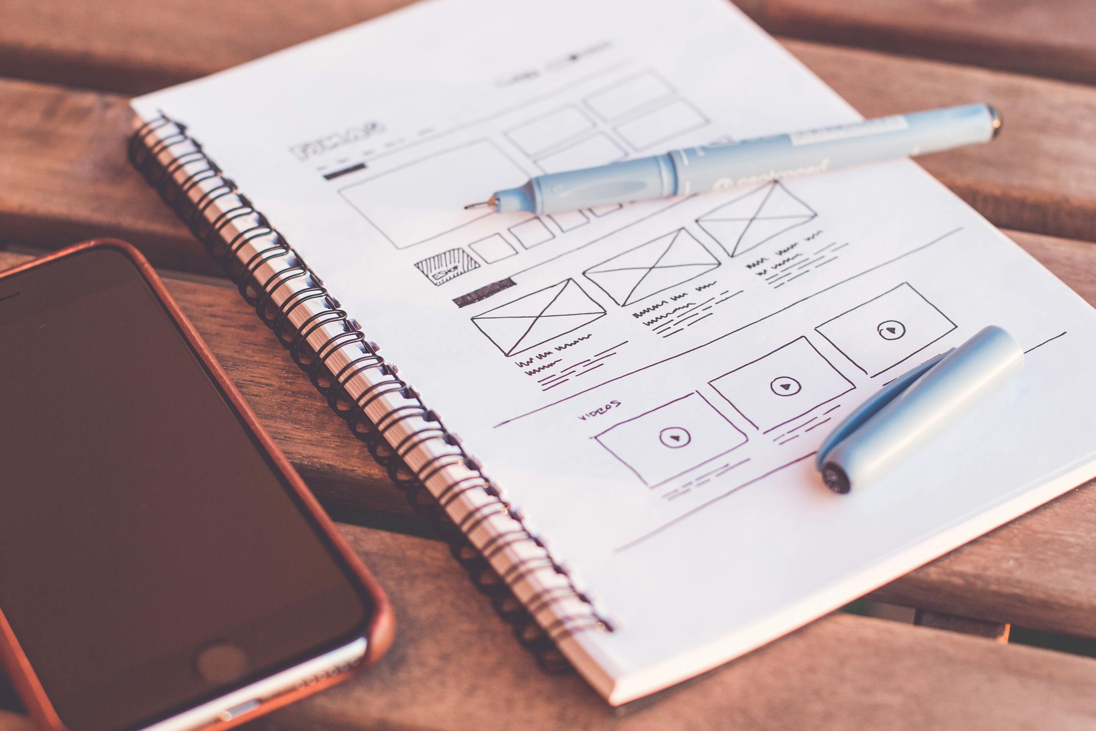 Boceto de wireframe de sitio web en libreta junto a un smartphone, ilustrando el proceso de diseño web